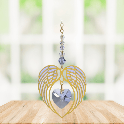 Gold angel wing heart suncatcher with light amethyst crystal heart hanging in a bright window

