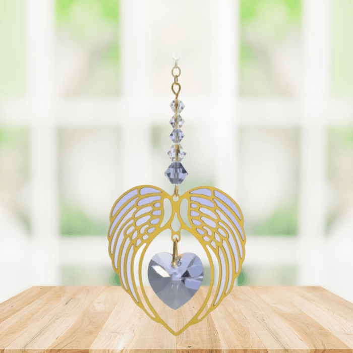 Gold angel wing heart suncatcher with light amethyst crystal heart hanging in a bright window
