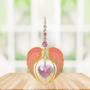 Gold angel wing heart suncatcher with rose pink crystal heart hanging in a bright window
