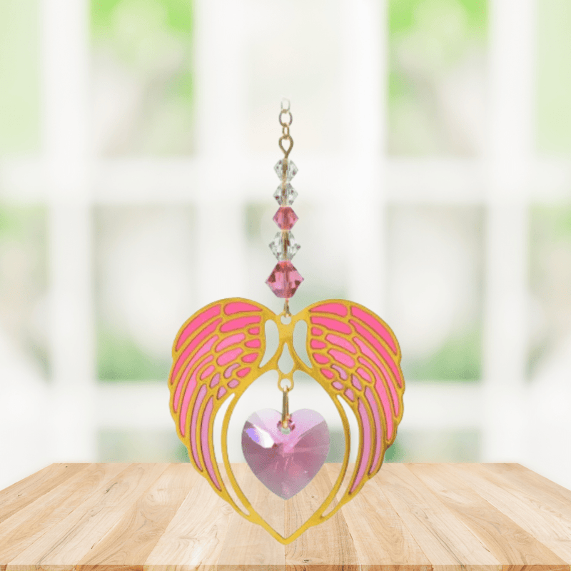 Gold angel wing heart suncatcher with rose pink crystal heart hanging in a bright window
