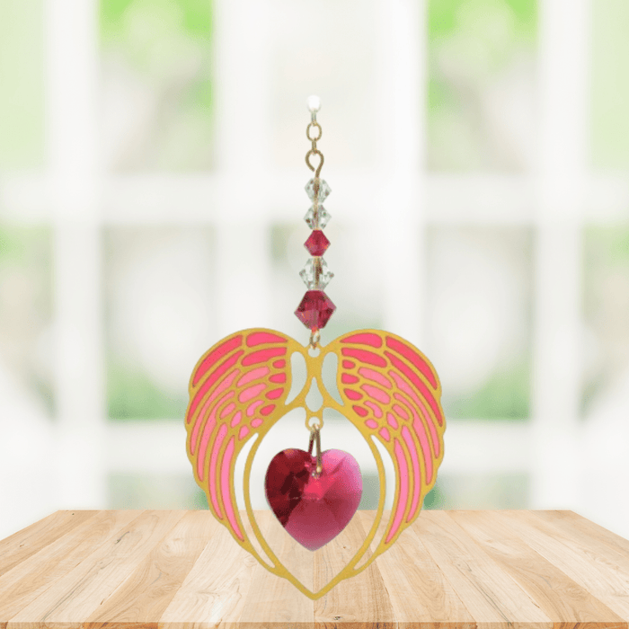 Gold angel wing heart suncatcher with ruby red crystal heart hanging in a bright window
