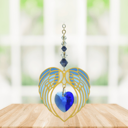 Gold angel wing heart suncatcher with sapphire blue crystal heart hanging in a bright window
