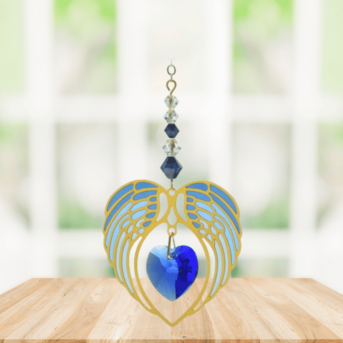 Gold angel wing heart suncatcher with sapphire blue crystal heart hanging in a bright window
