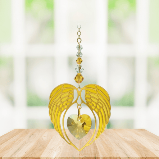 Gold angel wing heart suncatcher with topaz crystal heart hanging in a bright window

