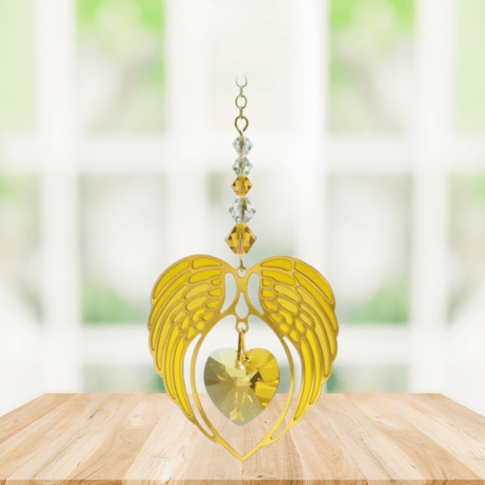 Gold angel wing heart suncatcher with topaz crystal heart hanging in a bright window
