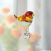Handmade amber-gold Goldfinch crystal suncatcher sparkling before blurred orange blooms

