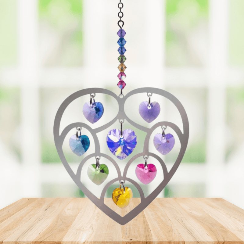 Handmade Heart of Hearts Confetti crystal suncatcher displayed on a wooden table before a bright window

