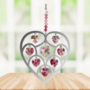 Handmade Heart of Hearts deep-rose crystal suncatcher displayed on a wooden table before a bright window

