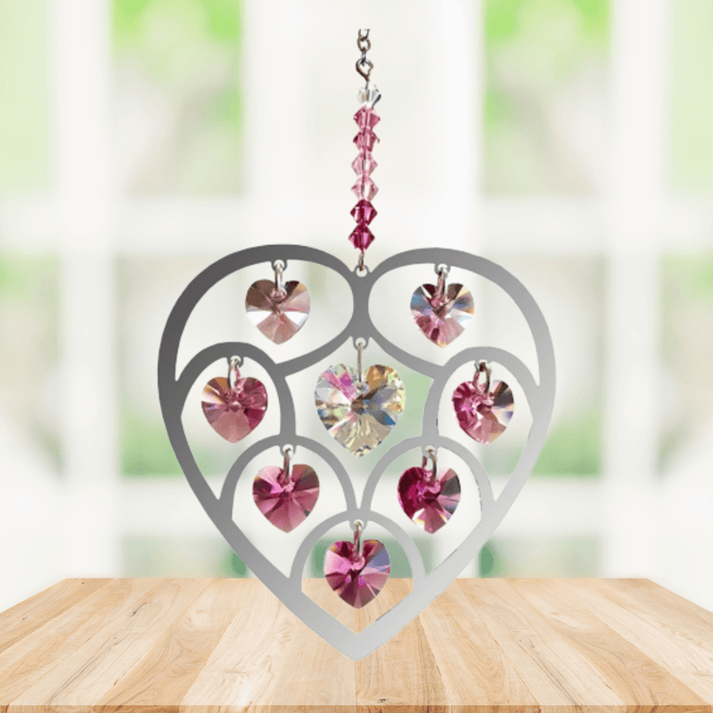 Handmade Heart of Hearts deep-rose crystal suncatcher displayed on a wooden table before a bright window

