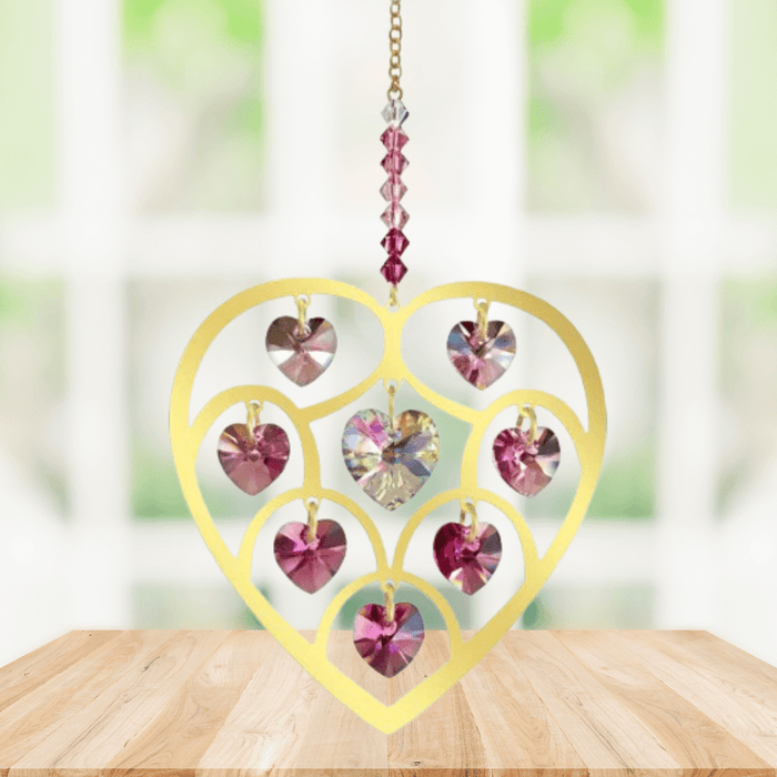 Handmade gold Heart of Hearts deep-rose crystal suncatcher displayed on a wooden table before a bright window

