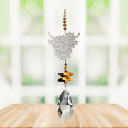 Wild Things Highland Cow Autumn Gold crystal suncatcher hanging in a window with amber beads, butterfly crystals and clear teardrop prism
