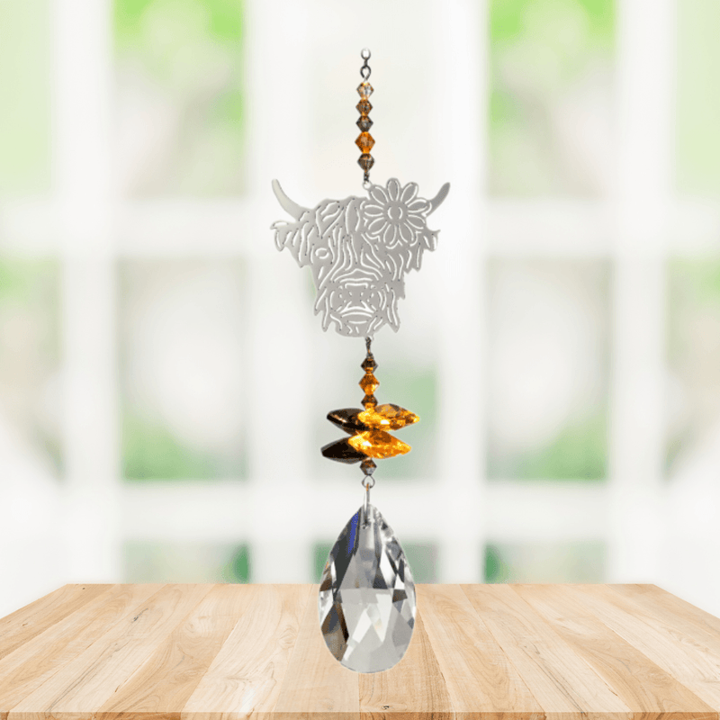 Wild Things Highland Cow Autumn Gold crystal suncatcher hanging in a window with amber beads, butterfly crystals and clear teardrop prism

