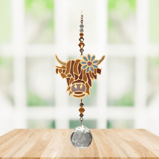 Wild Things Highland Cow Brown crystal suncatcher hanging in front of a window with amber beads and clear crystal prism