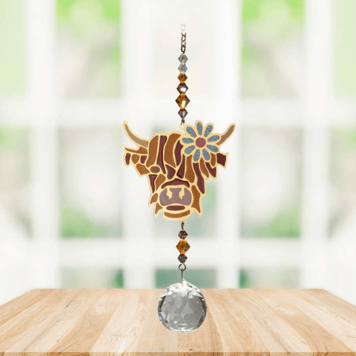 Wild Things Highland Cow Brown crystal suncatcher hanging in front of a window with amber beads and clear crystal prism