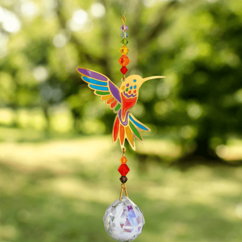 Hummingbird Rainbow Crystal Suncatcher catching garden sunlight – vivid bird motif, jewel-tone beads and 20 mm prism scattering rainbow light.

