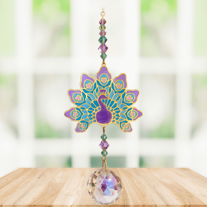 Peacock Purple Crystal Suncatcher hanging in a sunny window; ornate purple peacock, emerald–amethyst beads and dazzling crystal ball.
