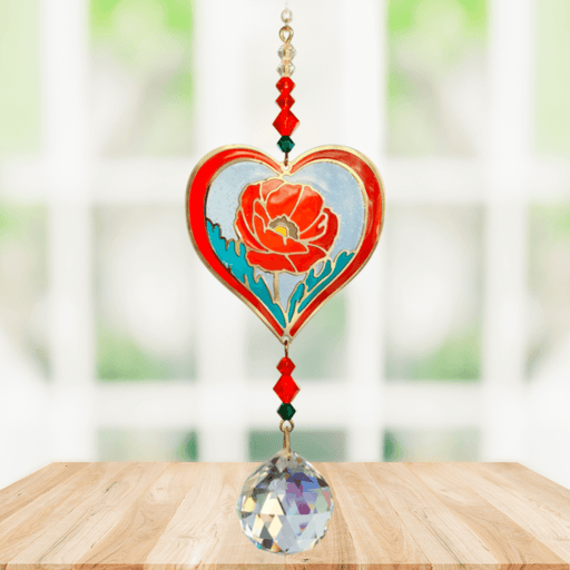 Poppy Rose Crystal Suncatcher hanging in a bright window; red-rimmed heart poppy motif, faceted crimson beads and sparkling crystal ball.
