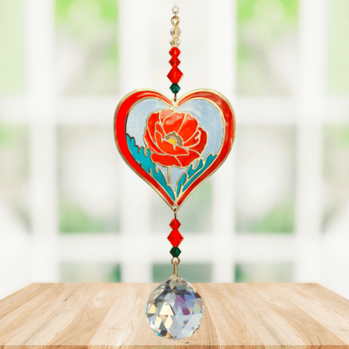 Poppy Rose Crystal Suncatcher hanging in a bright window; red-rimmed heart poppy motif, faceted crimson beads and sparkling crystal ball.

