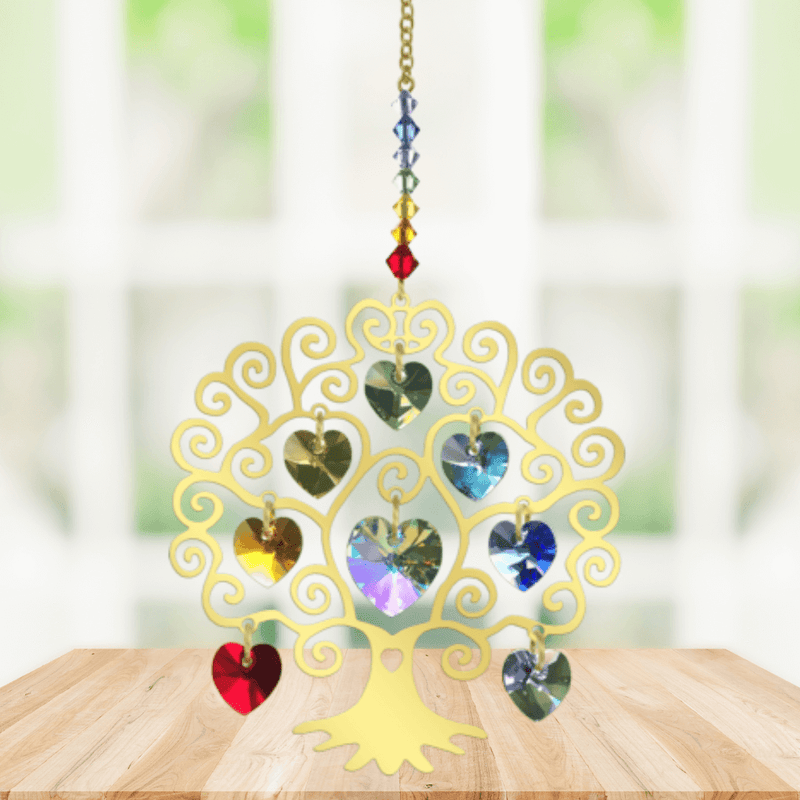 Handmade gold Tree of Life Chakra crystal suncatcher displayed on a wooden table before a bright window

