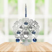 Polished metal Tree of Life winter suncatcher with blue crystal heart drops displayed on a wooden table

