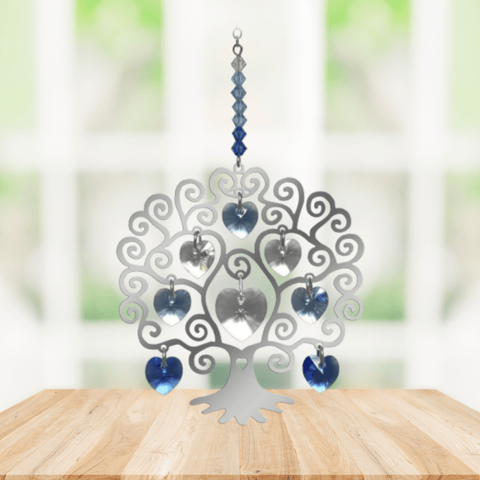 Polished metal Tree of Life winter suncatcher with blue crystal heart drops displayed on a wooden table

