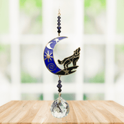 Wolf in Moon – Moonlight Crystal Suncatcher hanging in a bright window; star-strewn blue crescent, howling wolf, sapphire beads and sparkling crystal ball.
