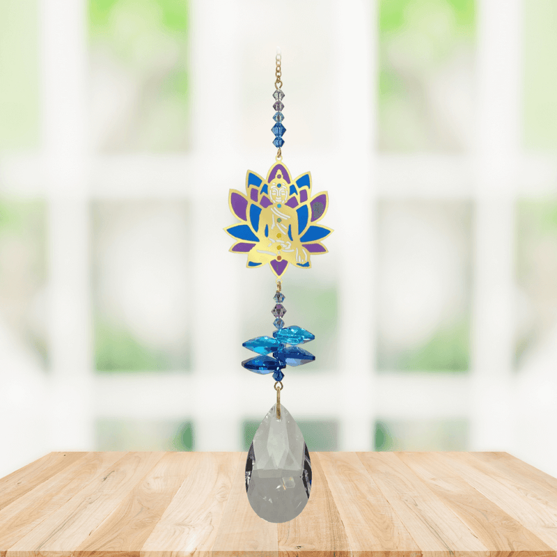Window Jewels Buddha moonlight crystal suncatcher hanging in a bright window, mirror-gold motif with blue crystals and clear crystal drop.