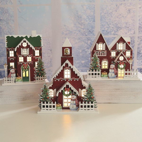 Wooden red townhouse with green roof and wreath, lit windows and snowman, 24 x 24cm, on white background.