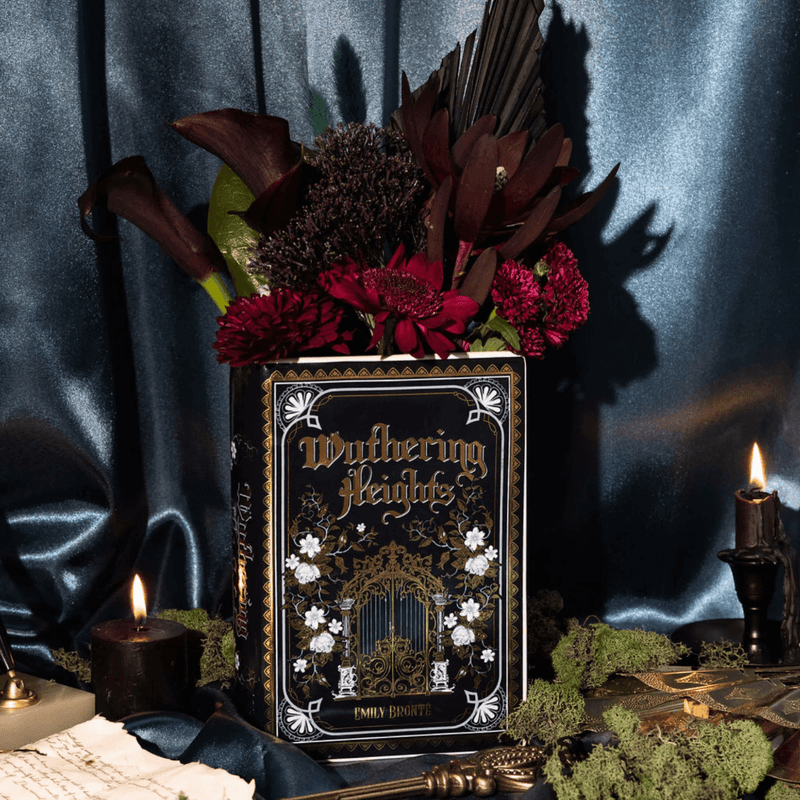Wuthering Heights ceramic book vase styled with dark red flowers, candles and moody blue fabric backdrop