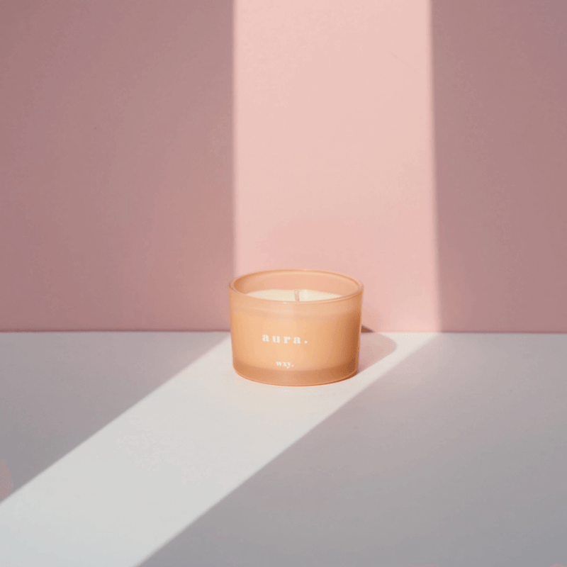 Peach frosted glass WXY Aura candle styled in soft light against a pale pink background.