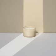 WXY bed candle in frosted pale grey glass styled in soft light with long shadows against a neutral backdrop.