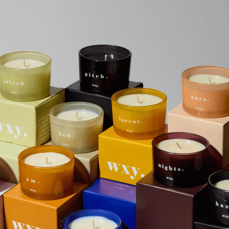 Assorted WXY coloured glass candles displayed together with branded boxes in a studio setting.