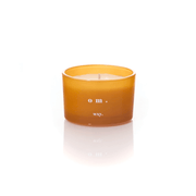 Amber glass WXY om candle with white wax and a centred wick on a white background.