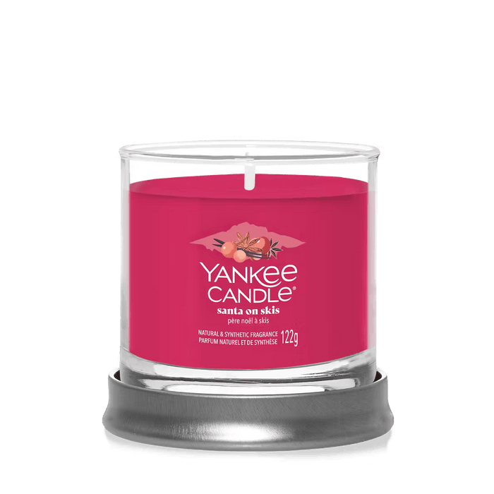 Santa on Skis small tumbler candle displayed on a metal stand