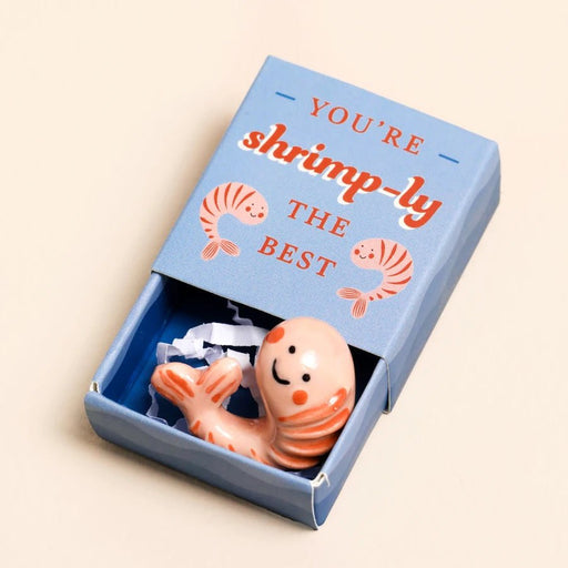 Open blue matchbox showing a mini ceramic shrimp token with You’re shrimp-ly the best printed on the lid